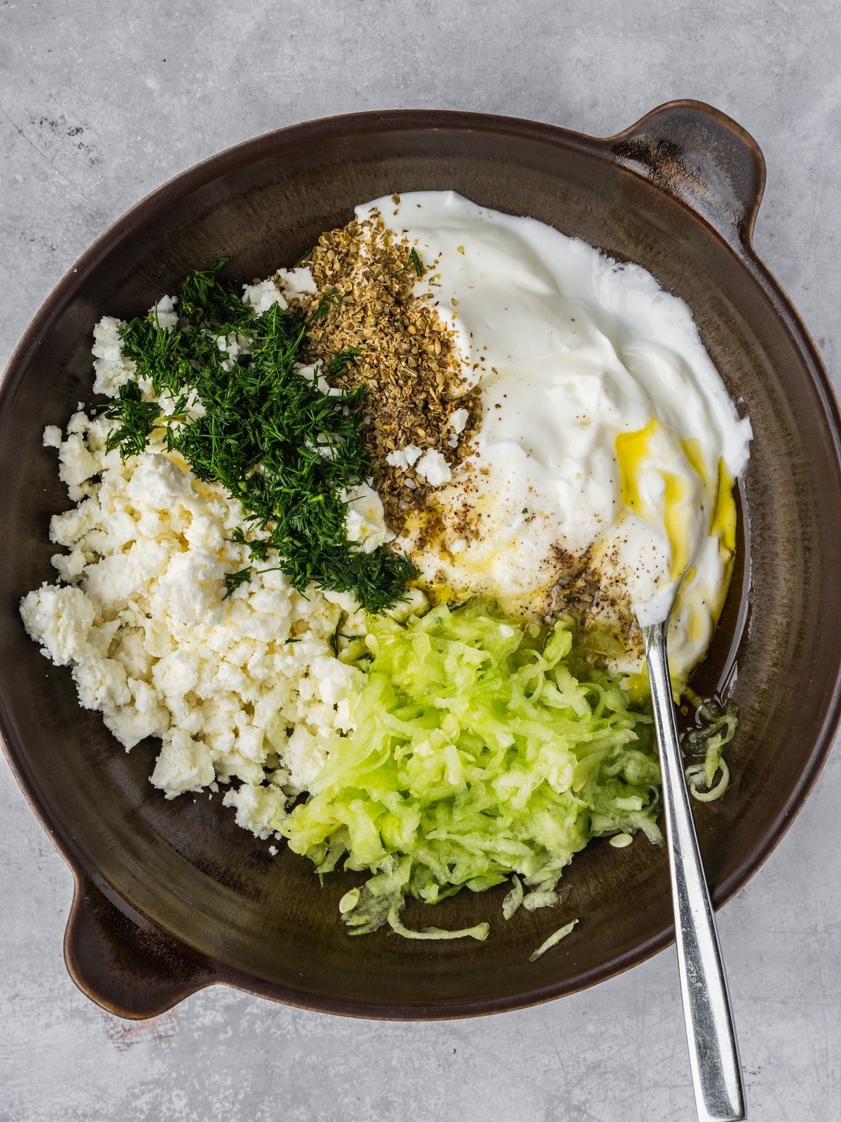 A bowl with yogurt, shredded cucumber, feta, herbs, lemon juice and olive oil
