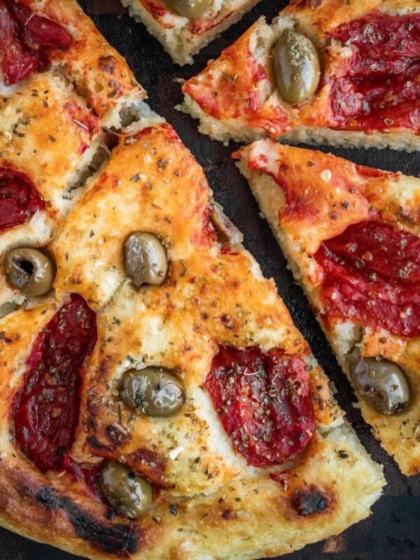 Focaccia Barese slices garnished with tomatoes, green olives and oregano on a wooden board.