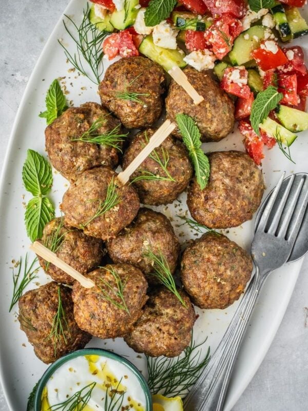 Greek Meatballs Keftedes on a platter garnished with fresh mint and dill with a side of Greek salad and yogurt dip.