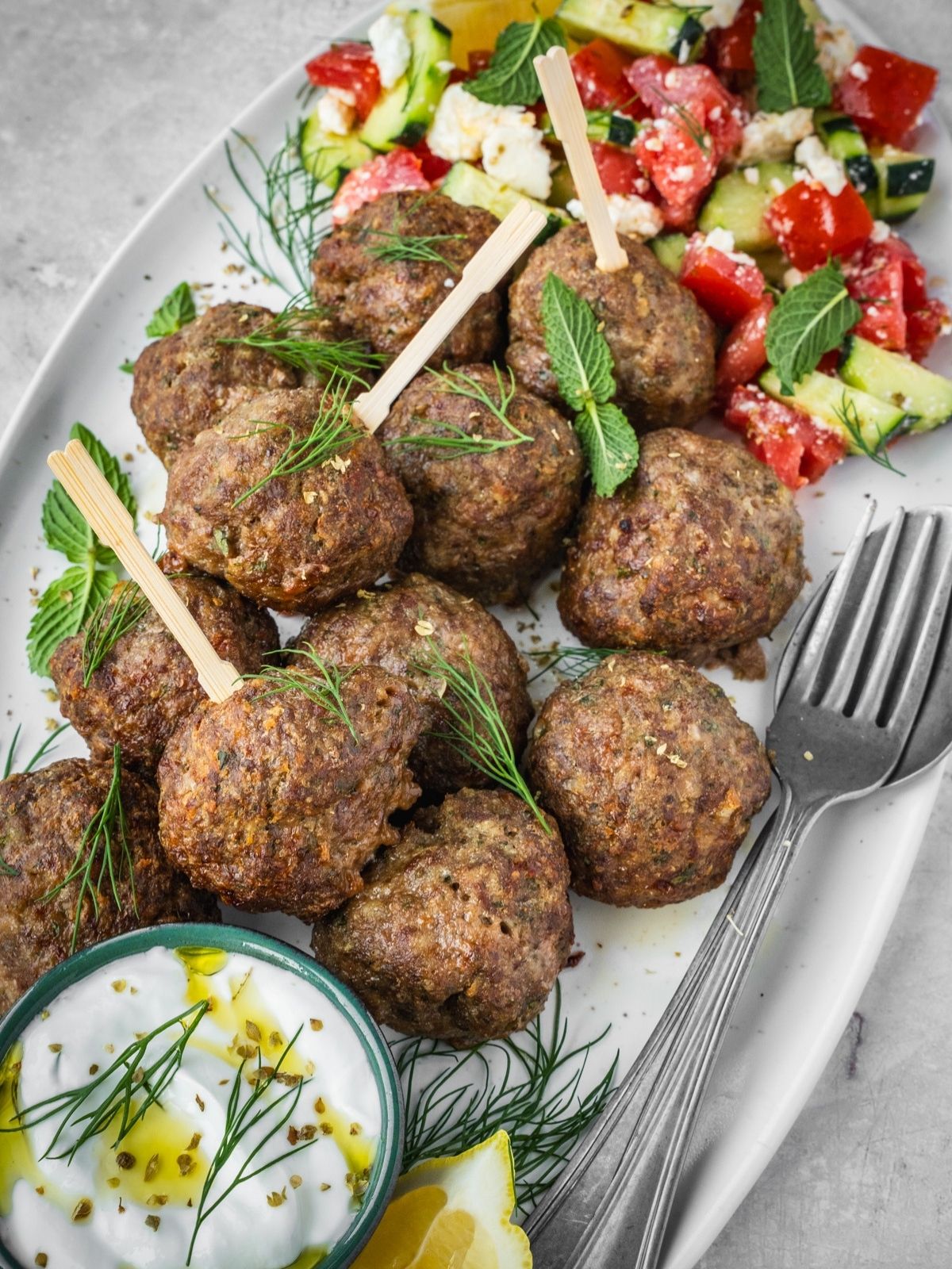 Greek Meatballs Keftedes on a platter garnished with fresh mint and dill with a side of Greek salad and yogurt dip.