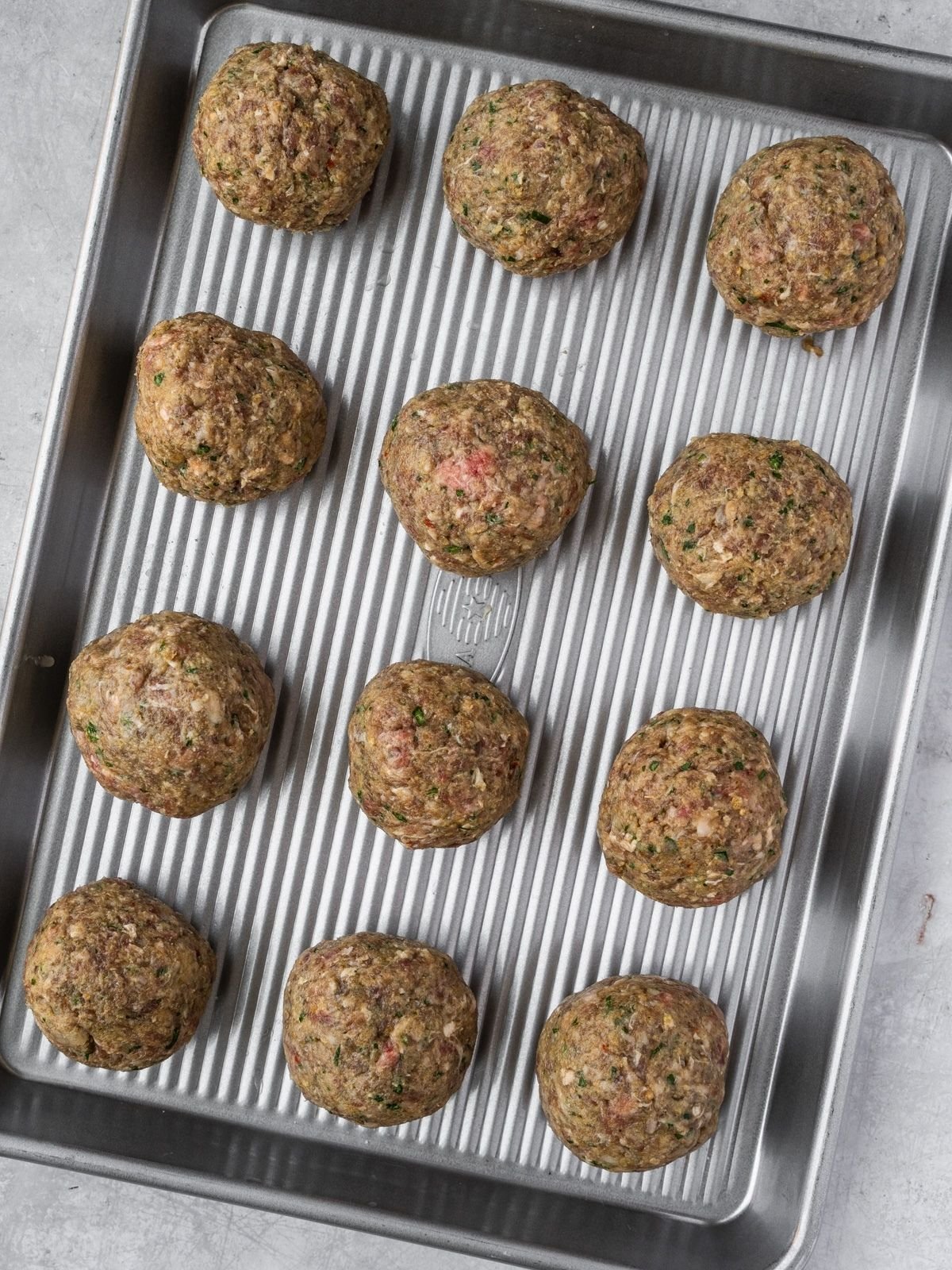 Twelve uncooked meatballs on a metal rimmed baking sheet.