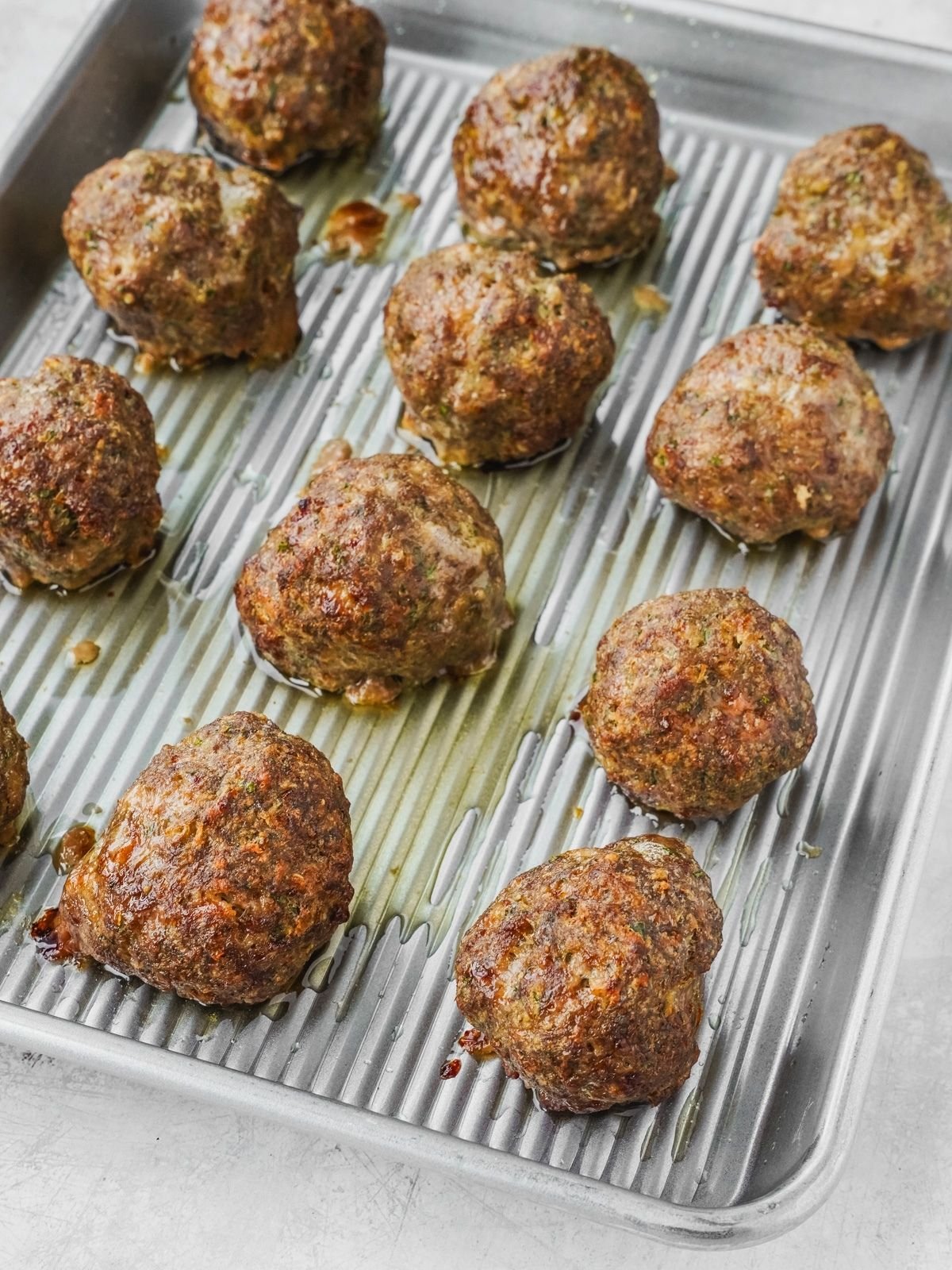 Twelve cooked meatballs on a metal rimmed baking sheet.