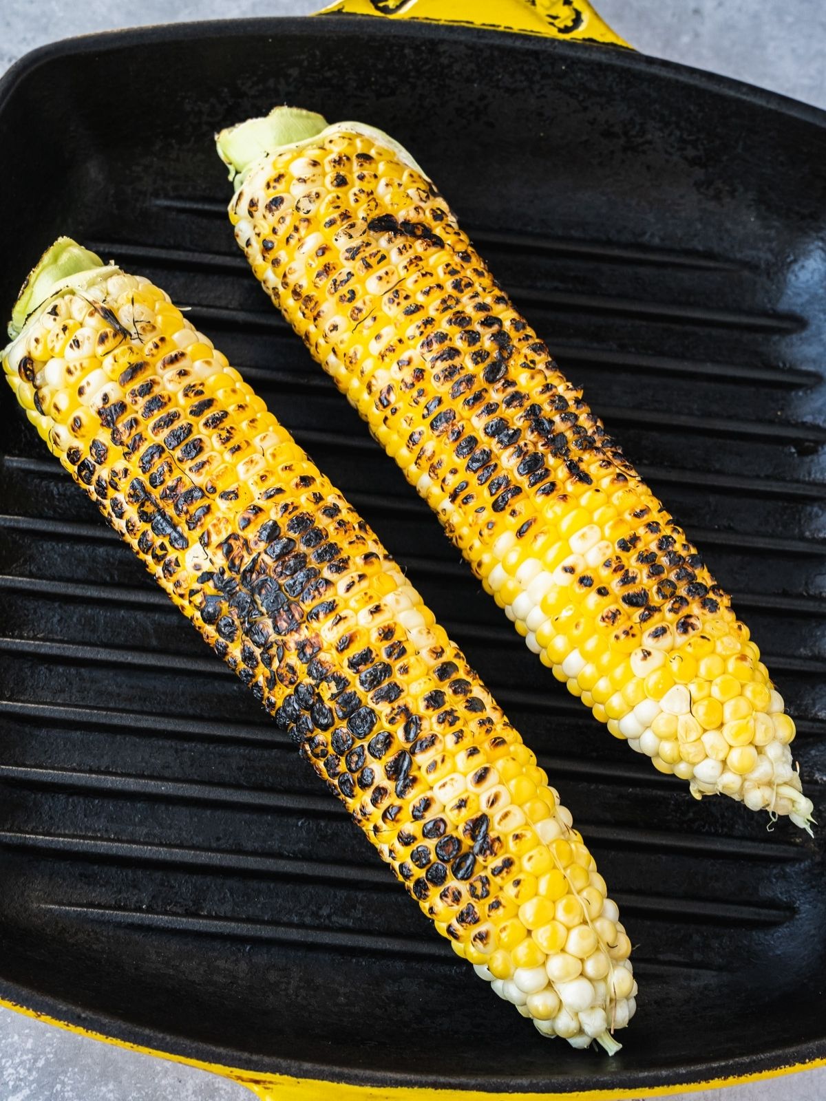 Two corn cobs grilling on an indoor grill pan.