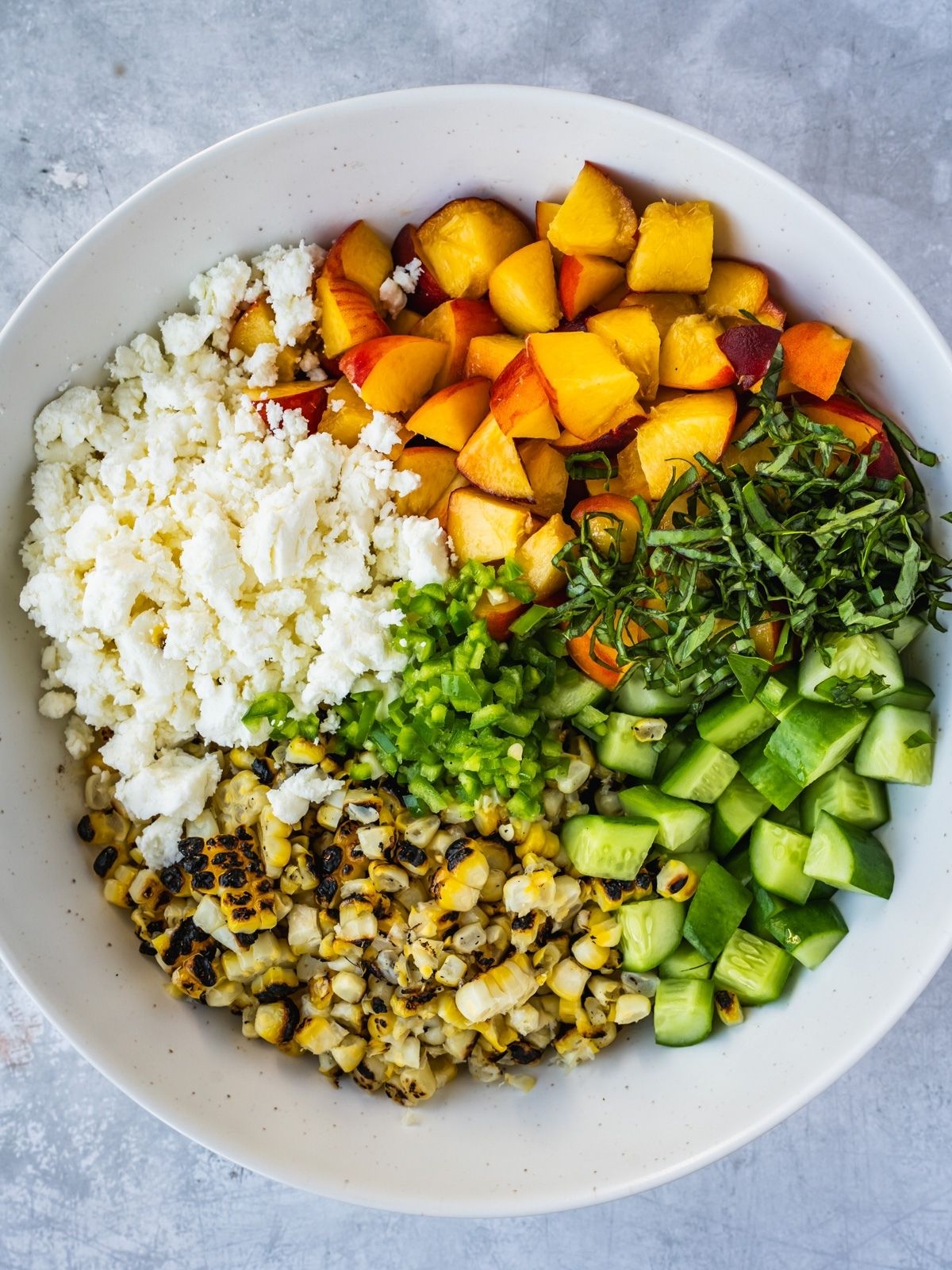 Salad bowl with sliced grilled corn kernels, diced cucumber, peaches, crumbled feta and herbs.