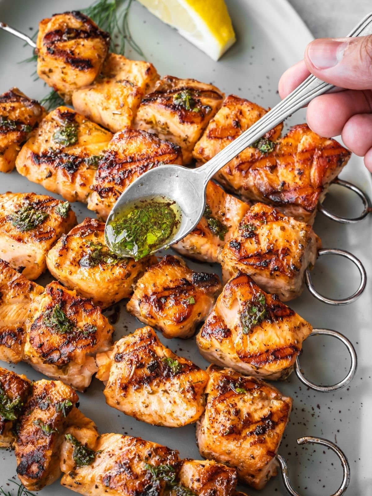 Spooning herb sauce over grilled Mediterranean salmon kabobs.