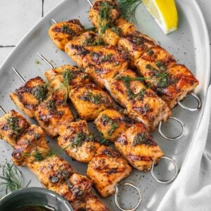 Grilled Mediterranean Salmon Kabobs on a platter garnished with dill and a side of lemon wedges.
