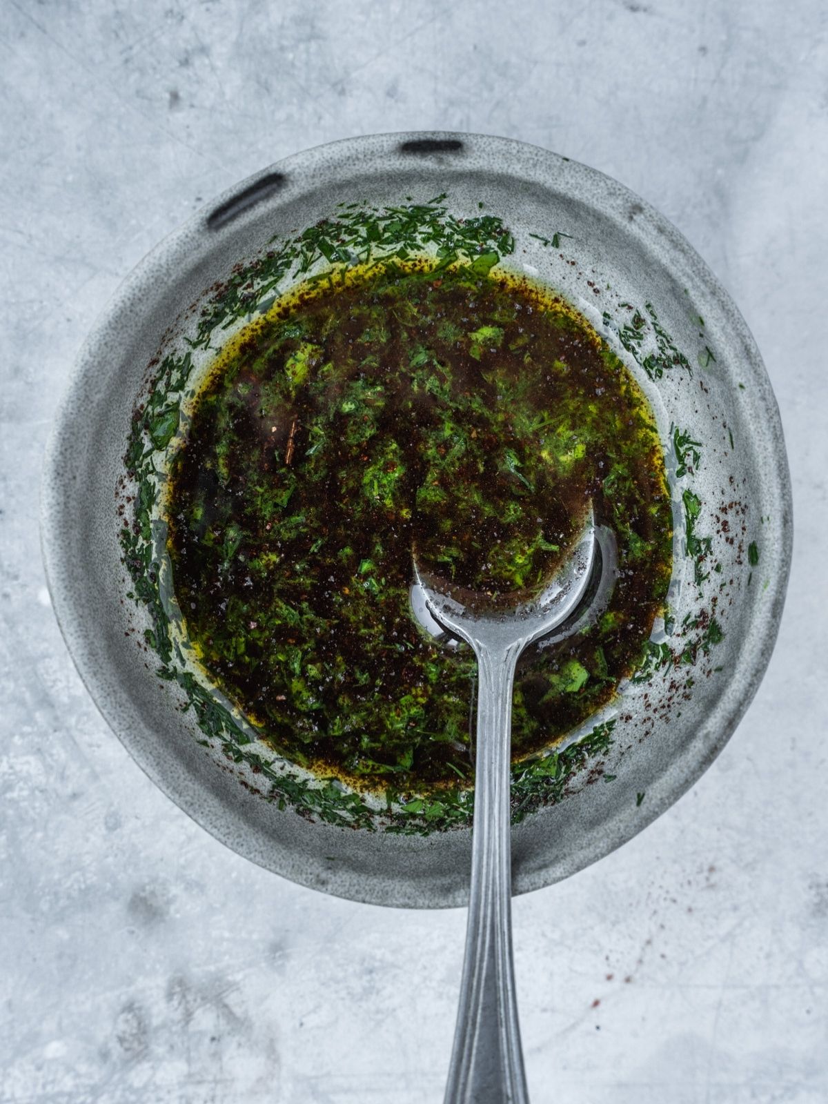 Small bowl with olive oil, lemon juice and chopped herbs.