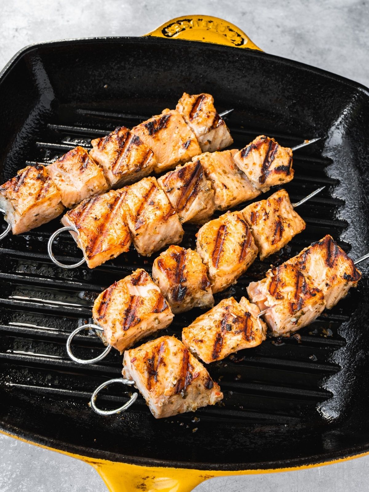 Salmon skewers getting grilled on a grill pan.