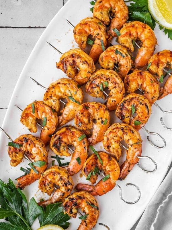 Grilled shrimp skewers laid out on a platter with parsley and lemon garnish.