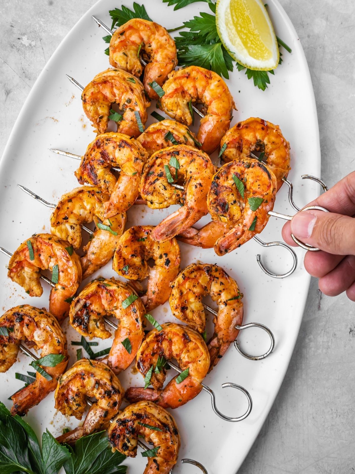 Grilled shrimp skewers laid out on a platter with parsley and lemon garnish.