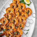 Grilled shrimp skewers laid out on a platter with parsley and lemon garnish.