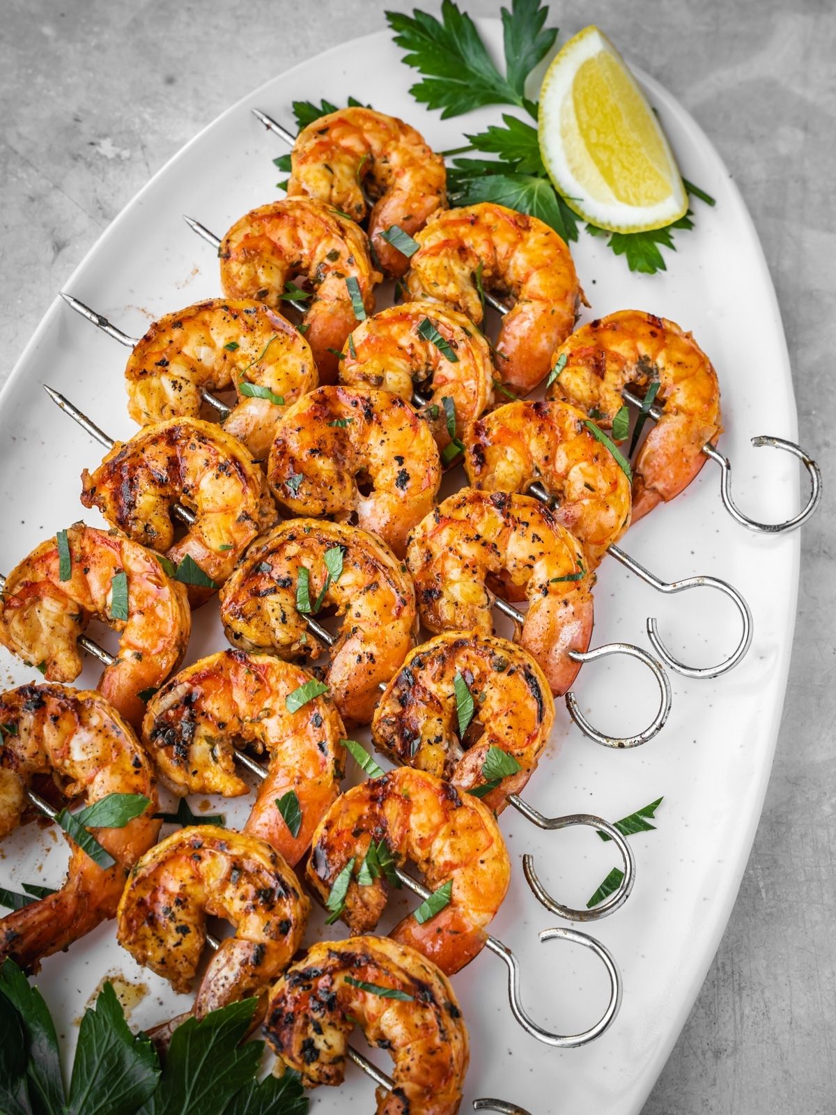 Grilled shrimp skewers laid out on a platter with parsley and lemon garnish.
