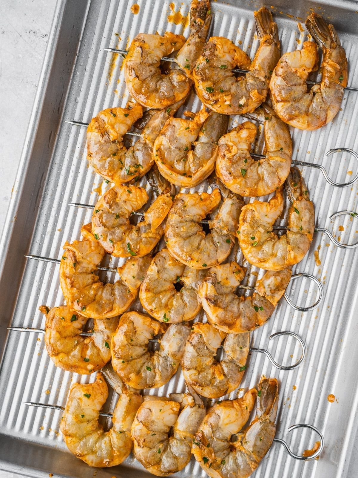 Marinated shrimp on skewers on a metal tray.