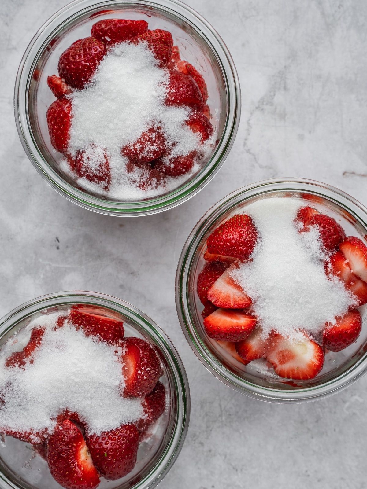 3 large glass containers with strawberries, sugar and a pinch of salt in each.
