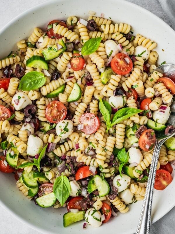 Mediterranean pasta salad with cherry tomatoes, cucumber, mozzarella balls, and olives in a large serving bowl.