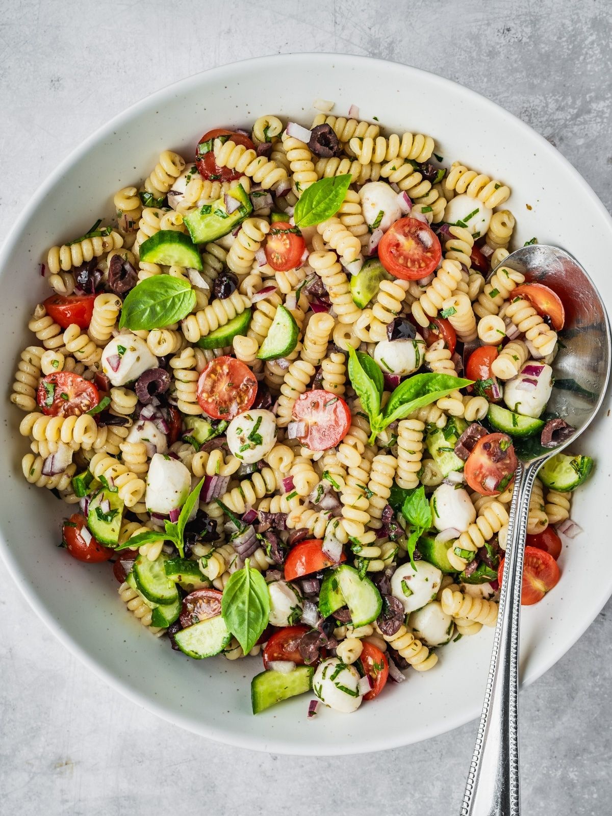 Mediterranean pasta salad with cherry tomatoes, cucumber, mozzarella balls, and olives in a large serving bowl.