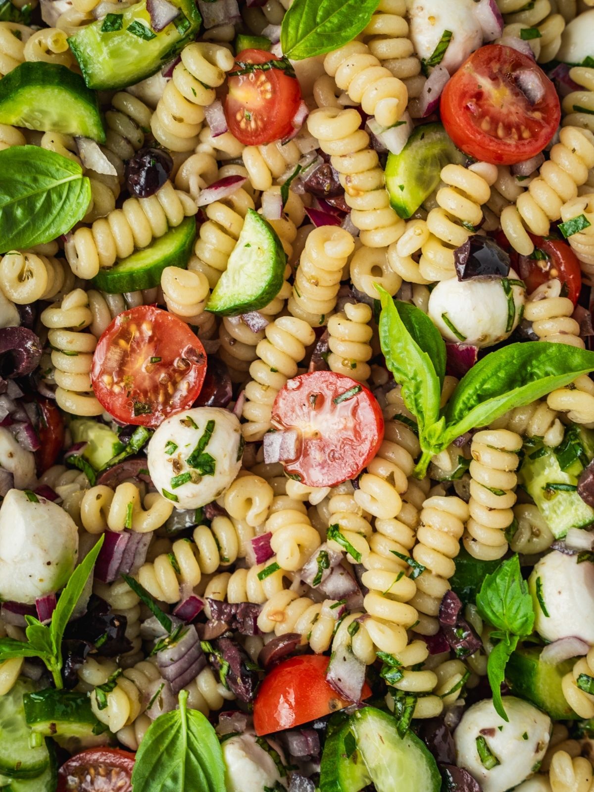 Mediterranean pasta salad with cherry tomatoes, cucumber, mozzarella balls, and olives.