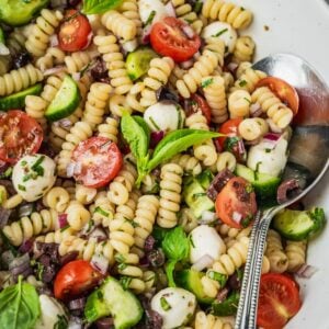 Mediterranean pasta salad with cherry tomatoes, cucumber, mozzarella balls, and olives in a large serving bowl.