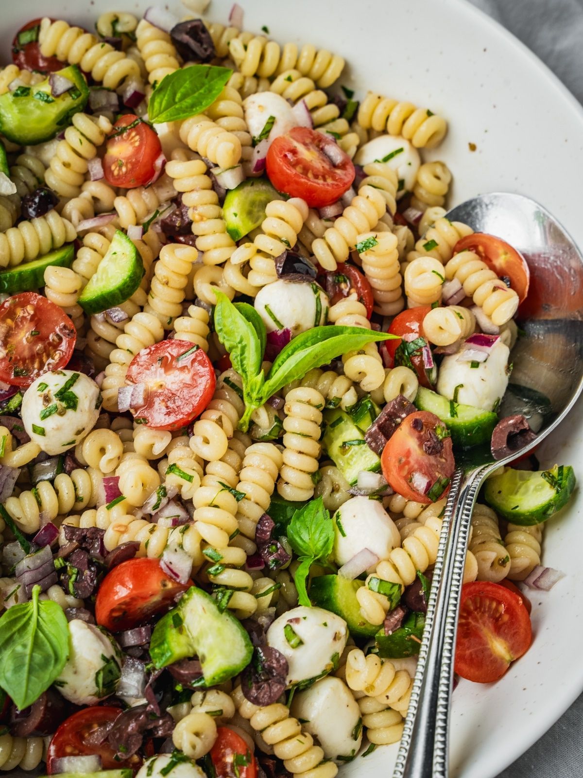 Mediterranean pasta salad with cherry tomatoes, cucumber, mozzarella balls, and olives in a large serving bowl.