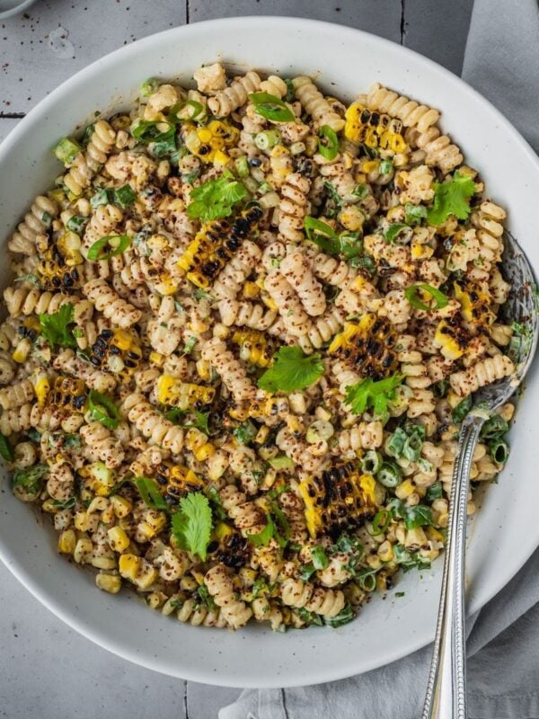 Mexican-inspired elote pasta salad in a large bowl garnished with tajin, fresh cilantro and chopped green onion.
