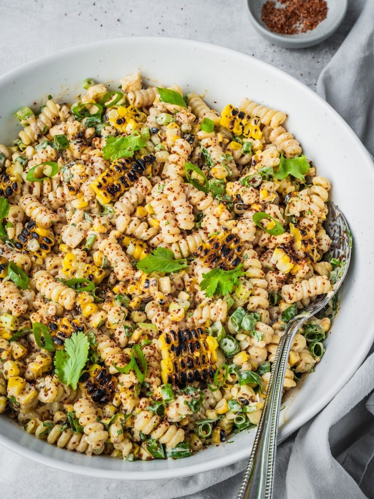 Mexican-inspired elote pasta salad in a large bowl garnished with tajin, fresh cilantro and chopped green onion.