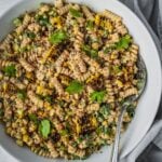 Mexican-inspired elote pasta salad in a large bowl garnished with tajin, fresh cilantro and chopped green onion.