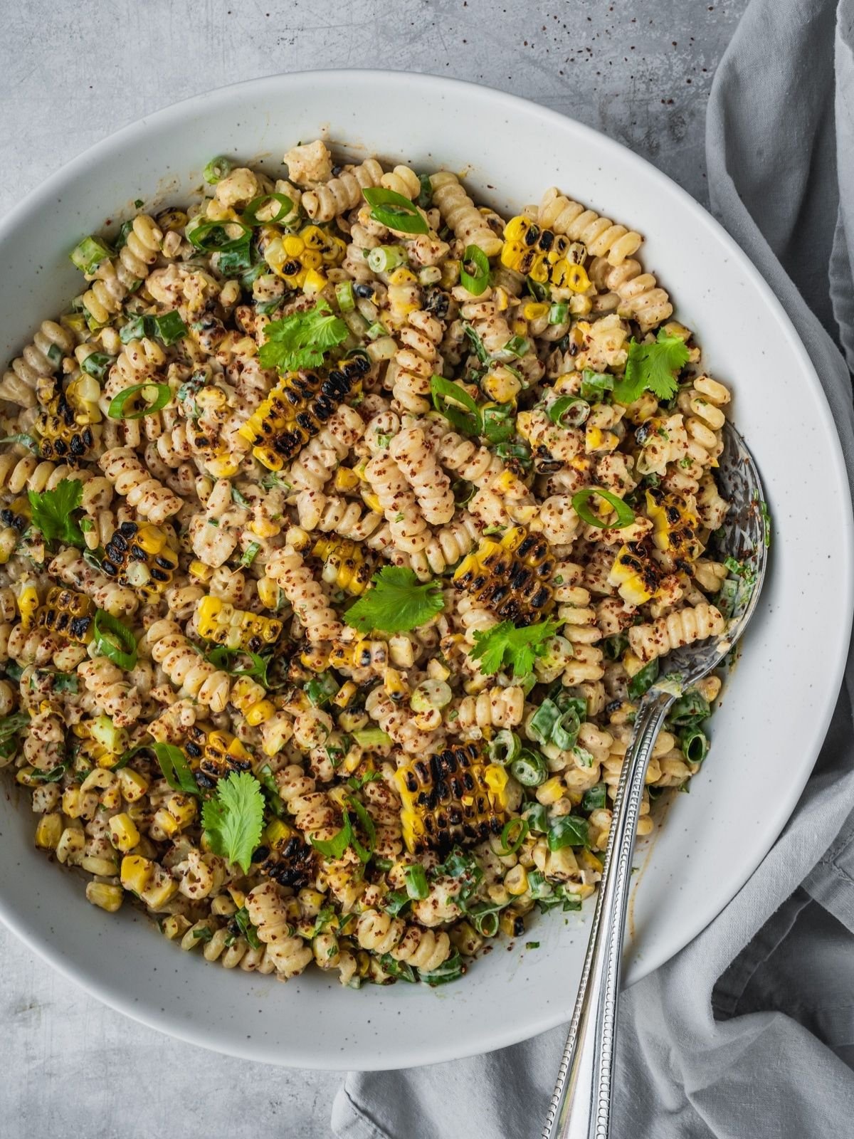 Mexican-inspired elote pasta salad in a large bowl garnished with tajin, fresh cilantro and chopped green onion.