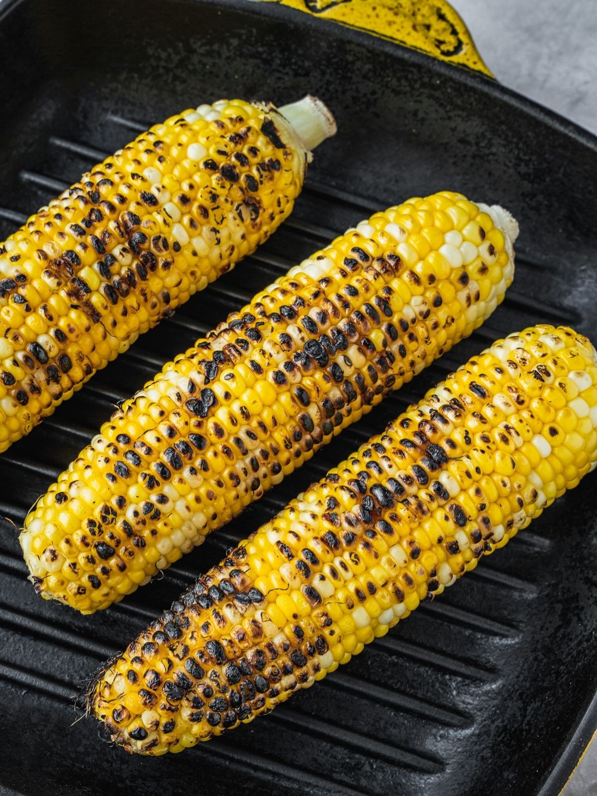 Three corn cobs grilling in a grill pan.