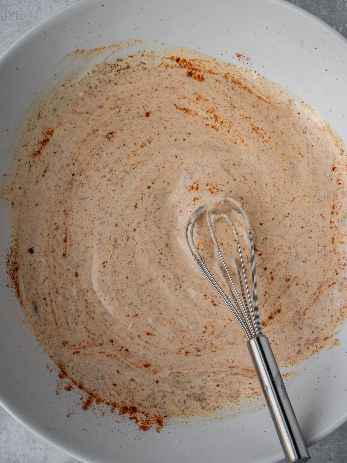 Salad dressing getting whisked in a large serving bowl.