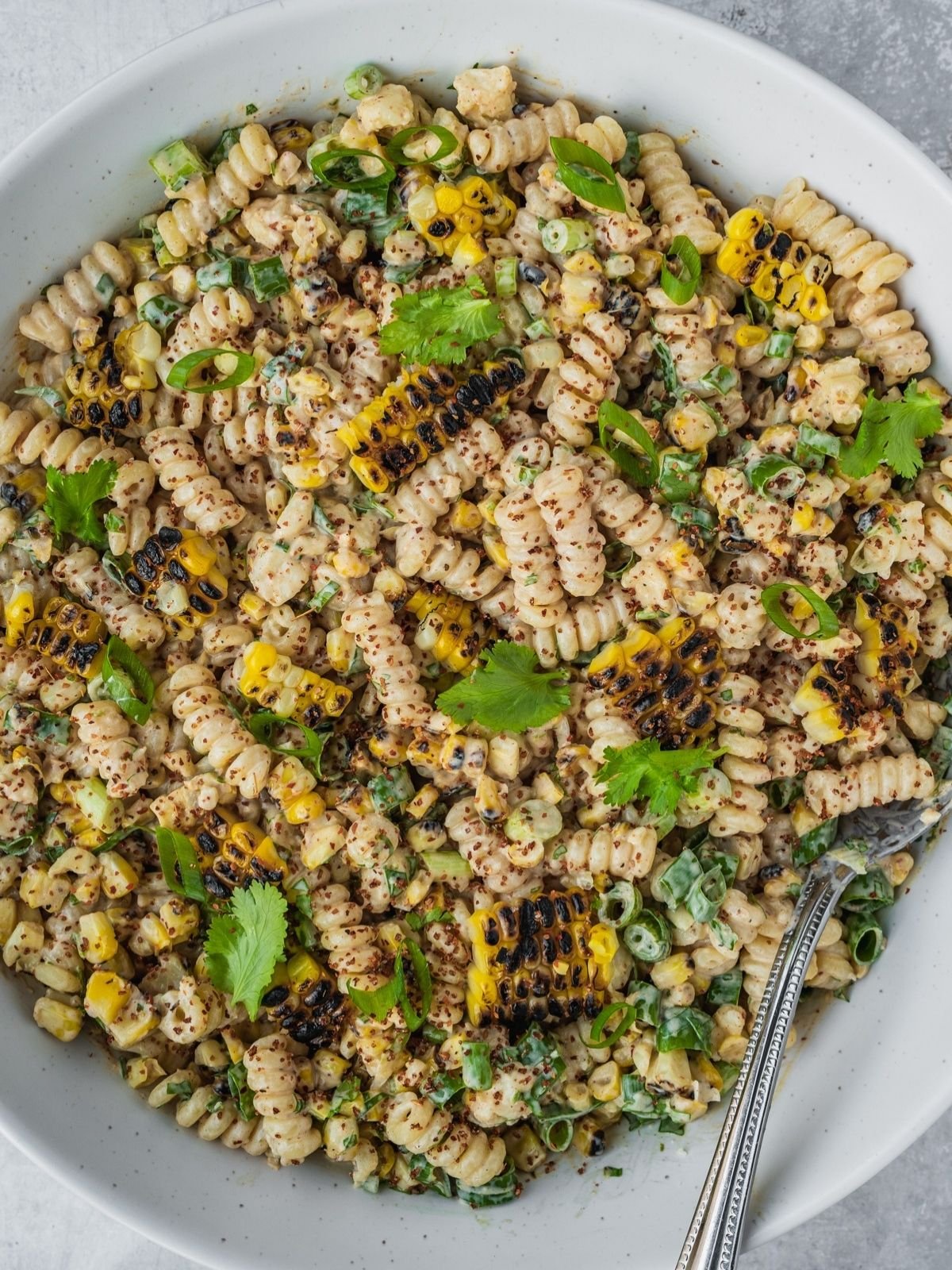 Elote pasta salad in a large bowl garnished with tajin, fresh cilantro and chopped green onion.