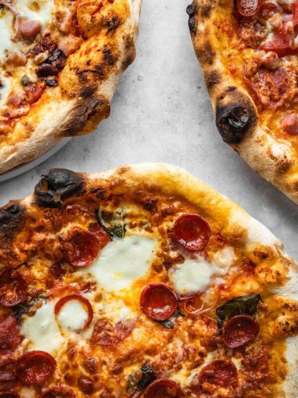 Three baked pizzas made with Overnight Biga Preferment Neapolitan Pizza Dough, garnished with cheese, pepperoni and herbs.