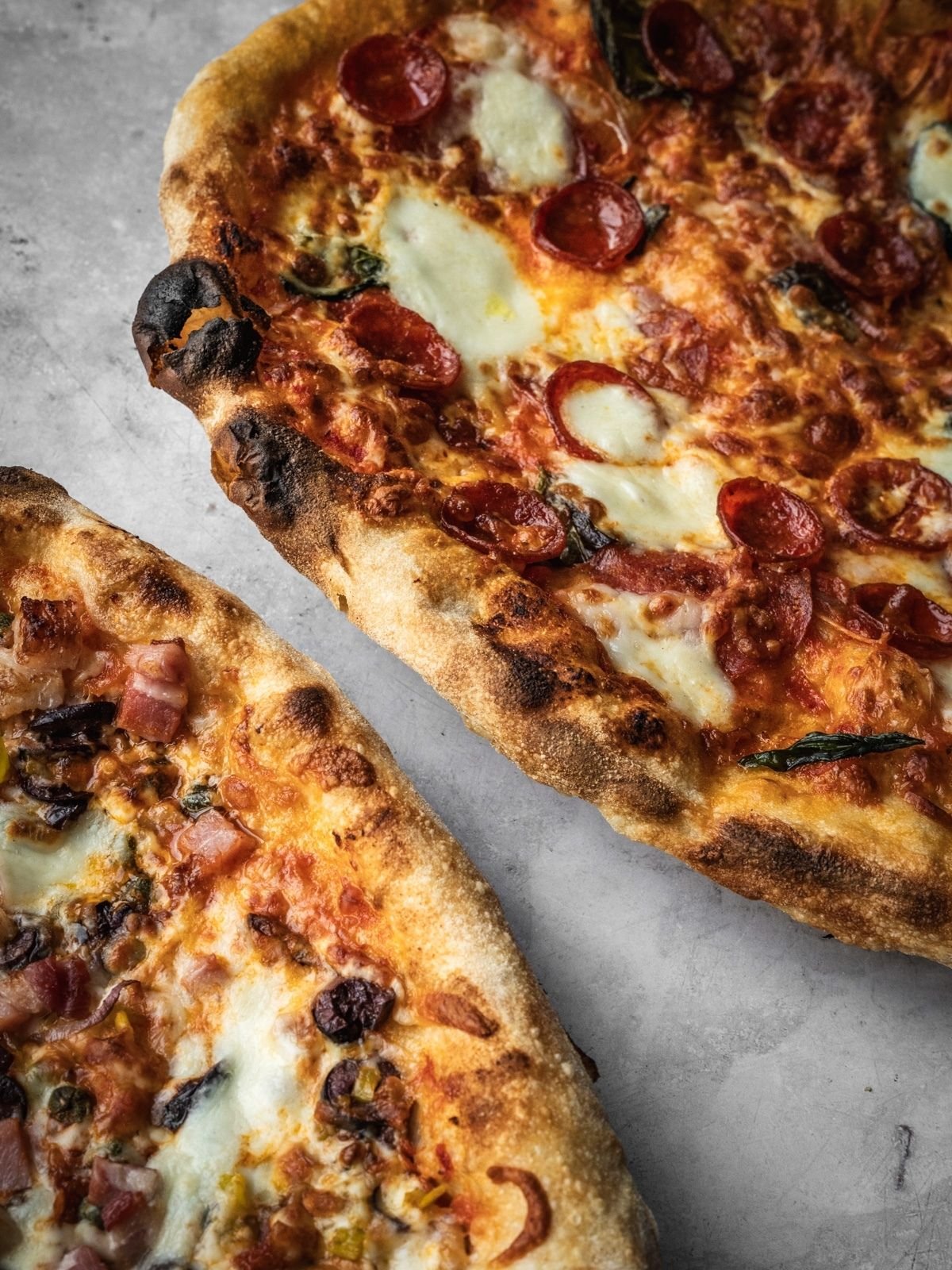 Two baked Neapolitan pizzas made with Biga Preferment dough, garnished with cheese, pepperoni and herbs.