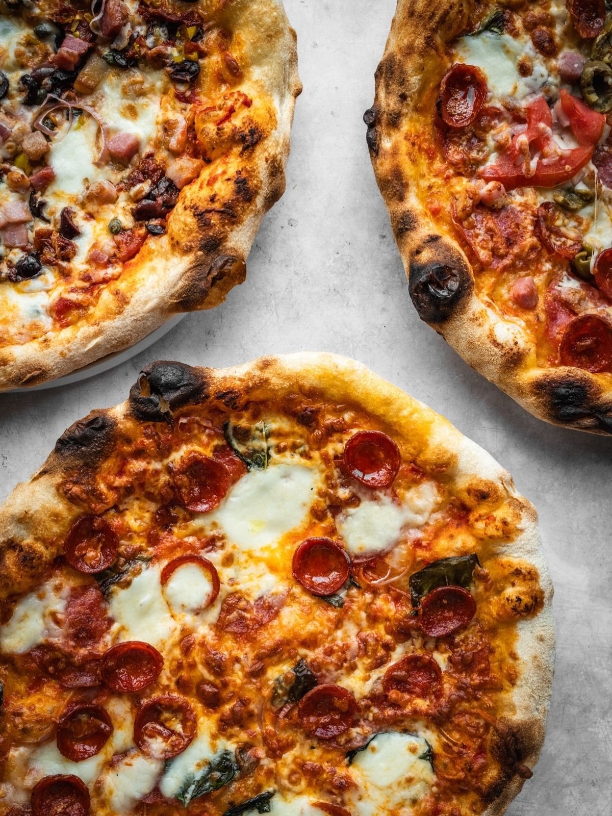 Three baked pizzas made with Overnight Biga Preferment Neapolitan Pizza Dough, garnished with cheese, pepperoni and herbs.