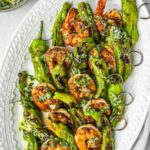 Grilled shrimp and shishito pepper skewers on a platter garnished with garlic and herb oil.
