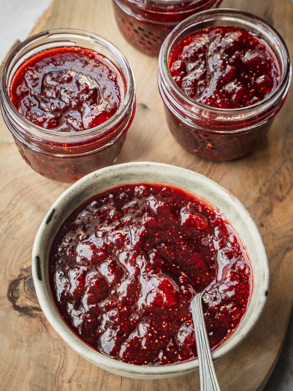 A bowl and mason jars with Strawberry Balsamic Black Pepper Jam.