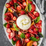 Strawberry Burrata Salad with fresh basil, sliced onion and heirloom tomatoes on a platter.