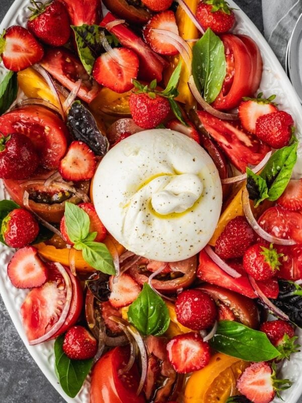 Strawberry Burrata Salad with fresh basil, sliced onion and heirloom tomatoes on a platter.