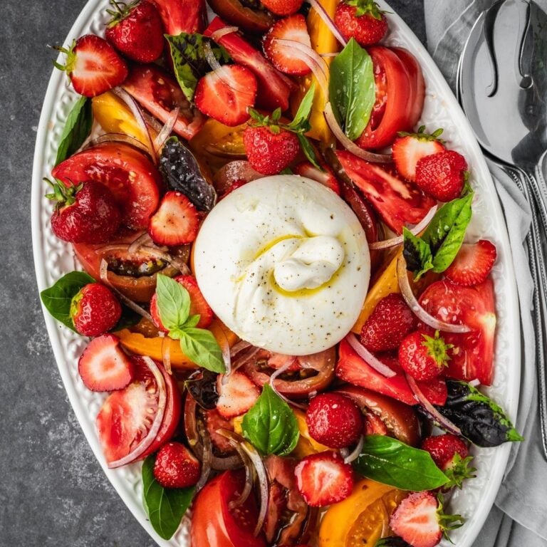Strawberry Burrata Salad with fresh basil, sliced onion and heirloom tomatoes on a platter.