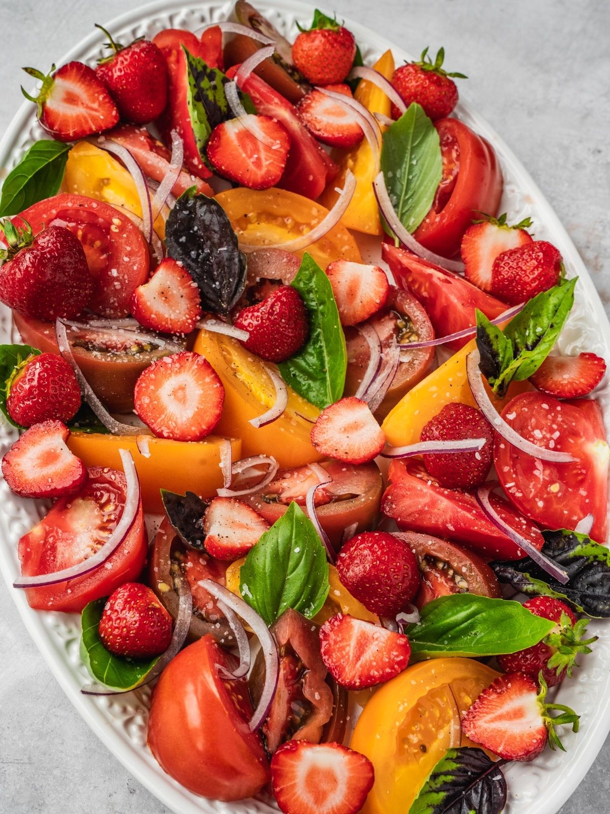 Platter with sliced tomatoes, strawberries, red onion and fresh basil.