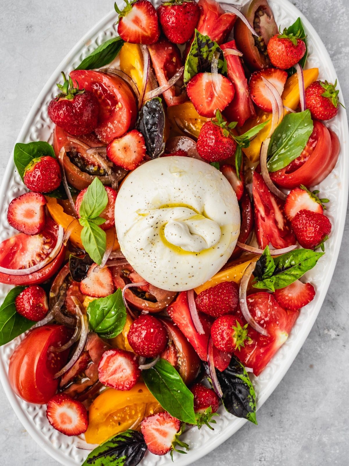 Strawberry Burrata Salad with fresh basil, sliced onion and heirloom tomatoes on a platter.