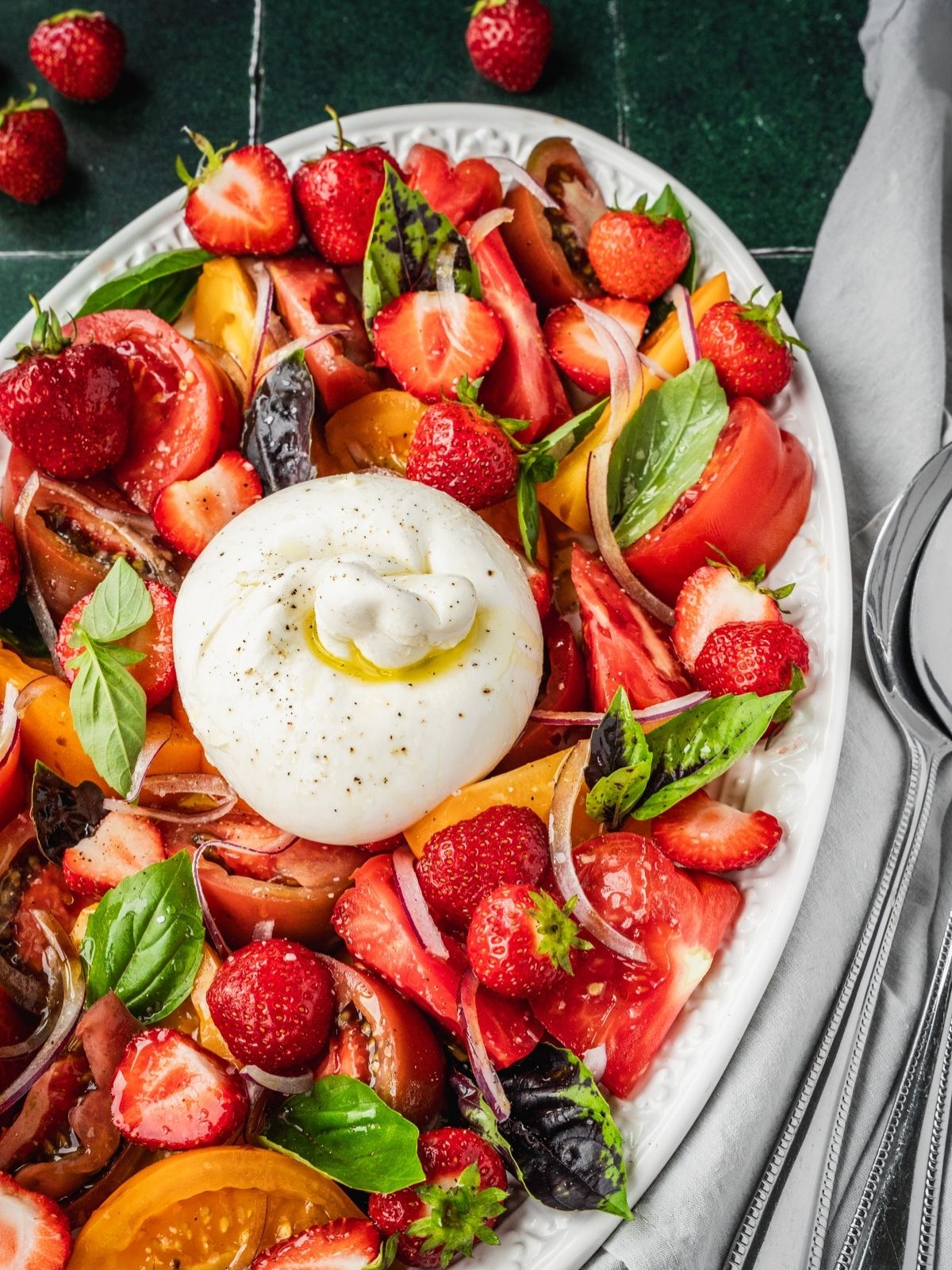 Strawberry Burrata Salad with fresh basil, sliced onion and heirloom tomatoes on a platter.
