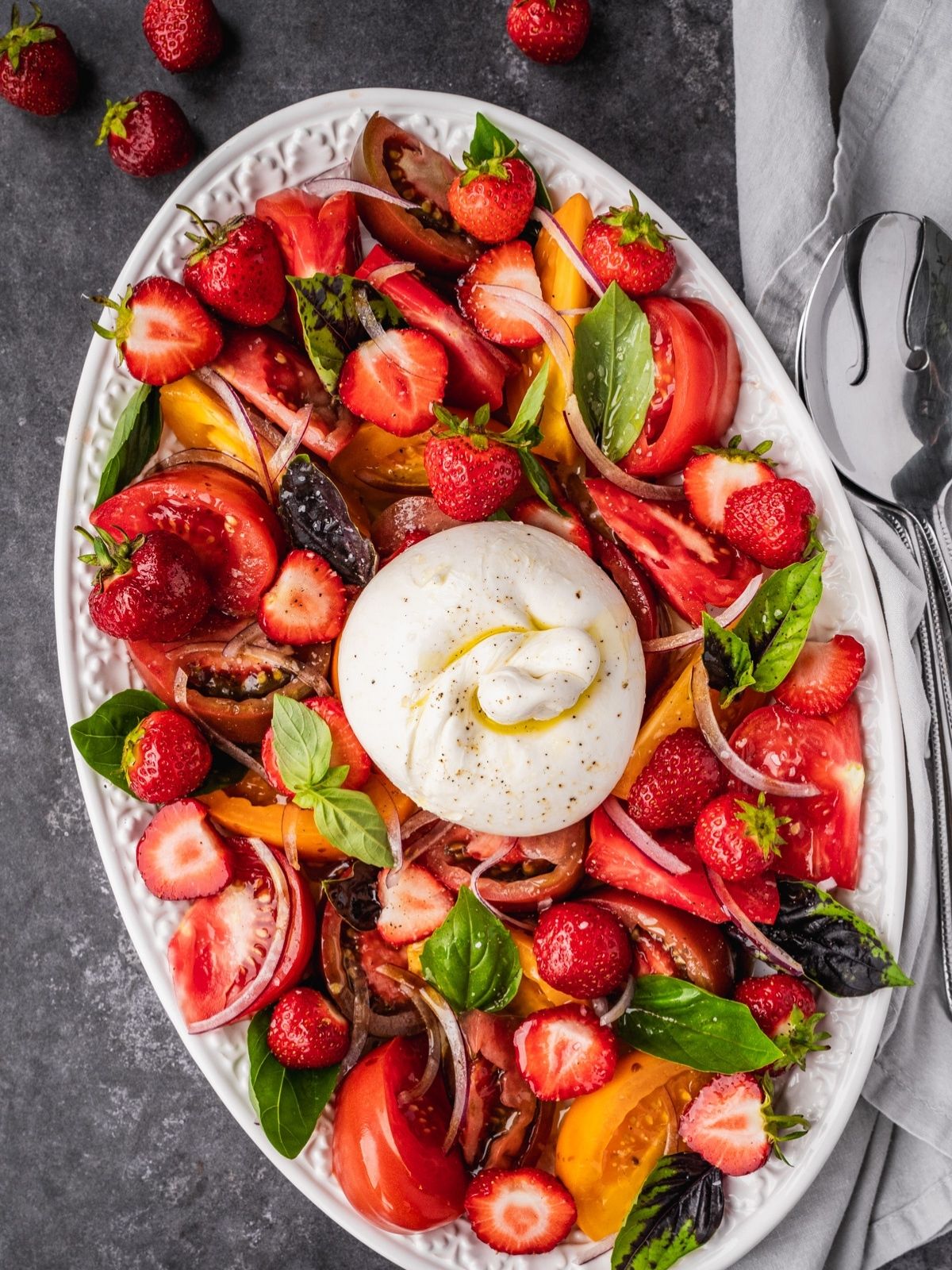 Strawberry Burrata Salad with fresh basil, sliced onion and heirloom tomatoes on a platter.