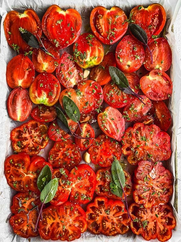 A baking sheet with open faced tomatoes seasoned with herbs, salt and olive oil.