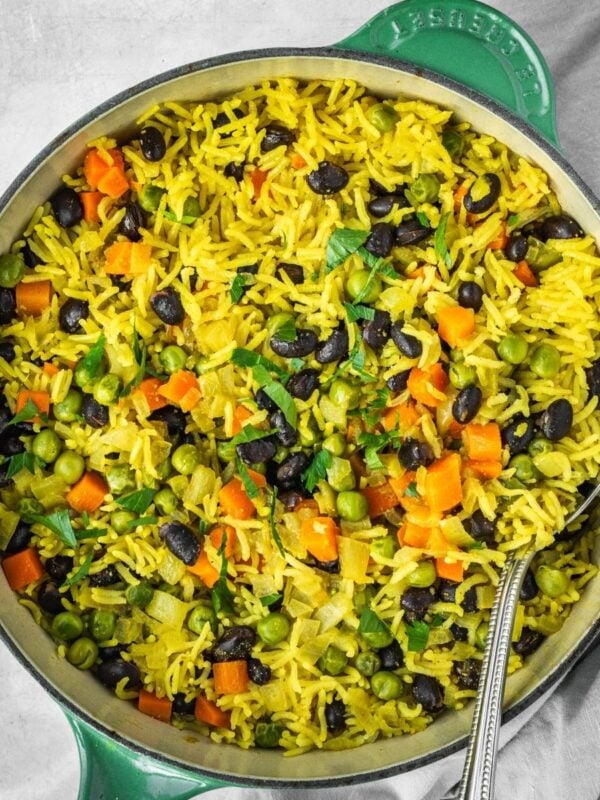 Middle Eastern Vegetable Rice Pilaf with peas, carrots and black beans, garnished with fresh parsley in a pot.