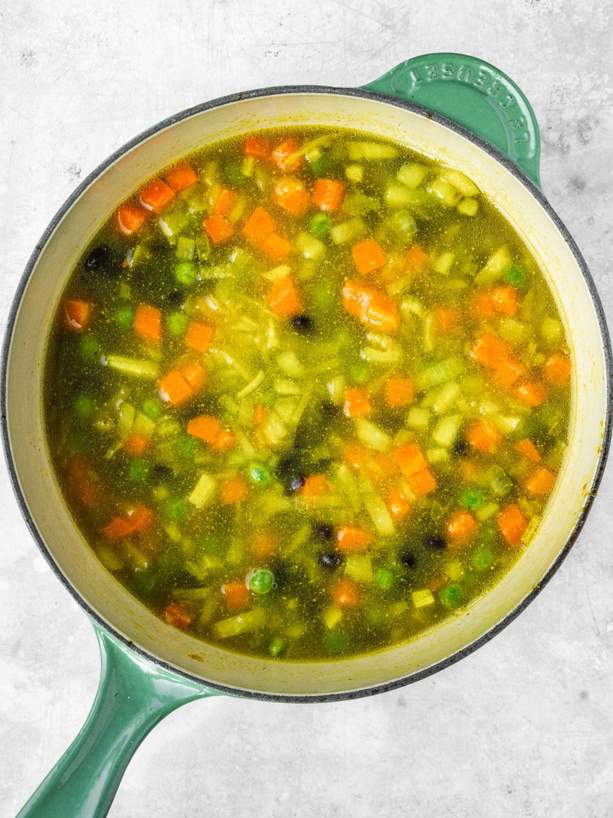 A pot with the fried aromatics, stock, peas, carrots, bean and rice before getting boiled.