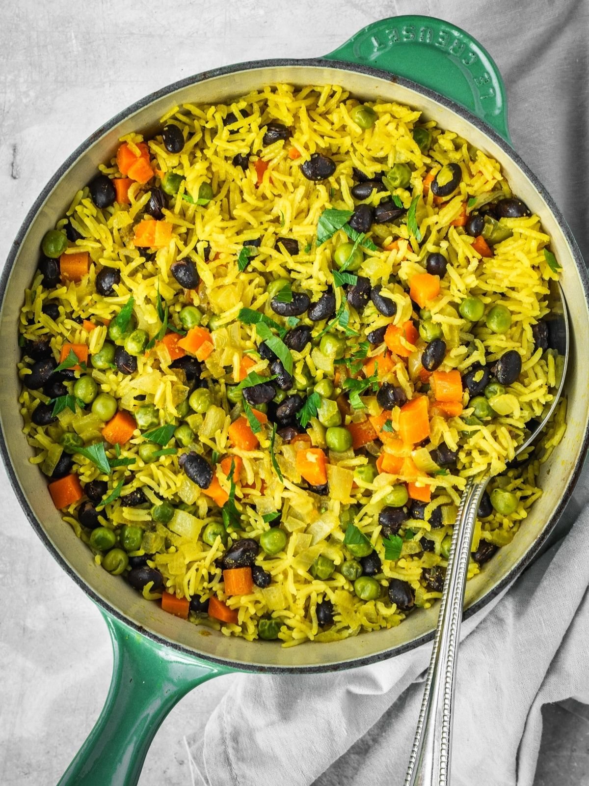 Middle Eastern Vegetable Rice Pilaf with peas, carrots and black beans, garnished with fresh parsley in a pot.