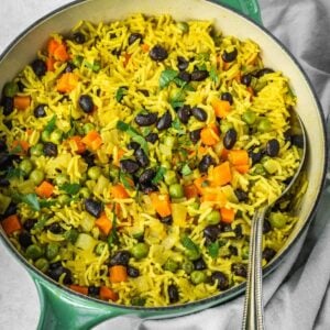 Middle Eastern Vegetable Rice Pilaf with peas, carrots and black beans, garnished with fresh parsley in a pot.
