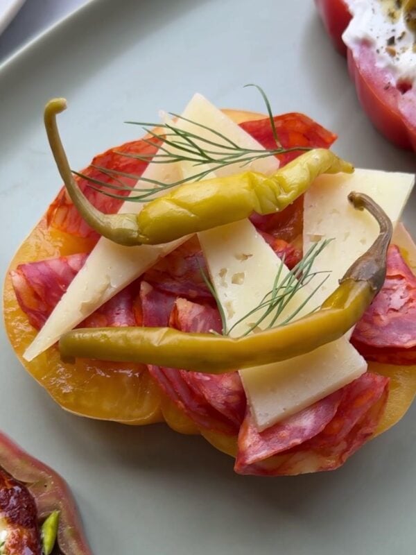 Slice of heirloom tomato with cheese, salami and peppers on top as part of a tomato flight on a platter.