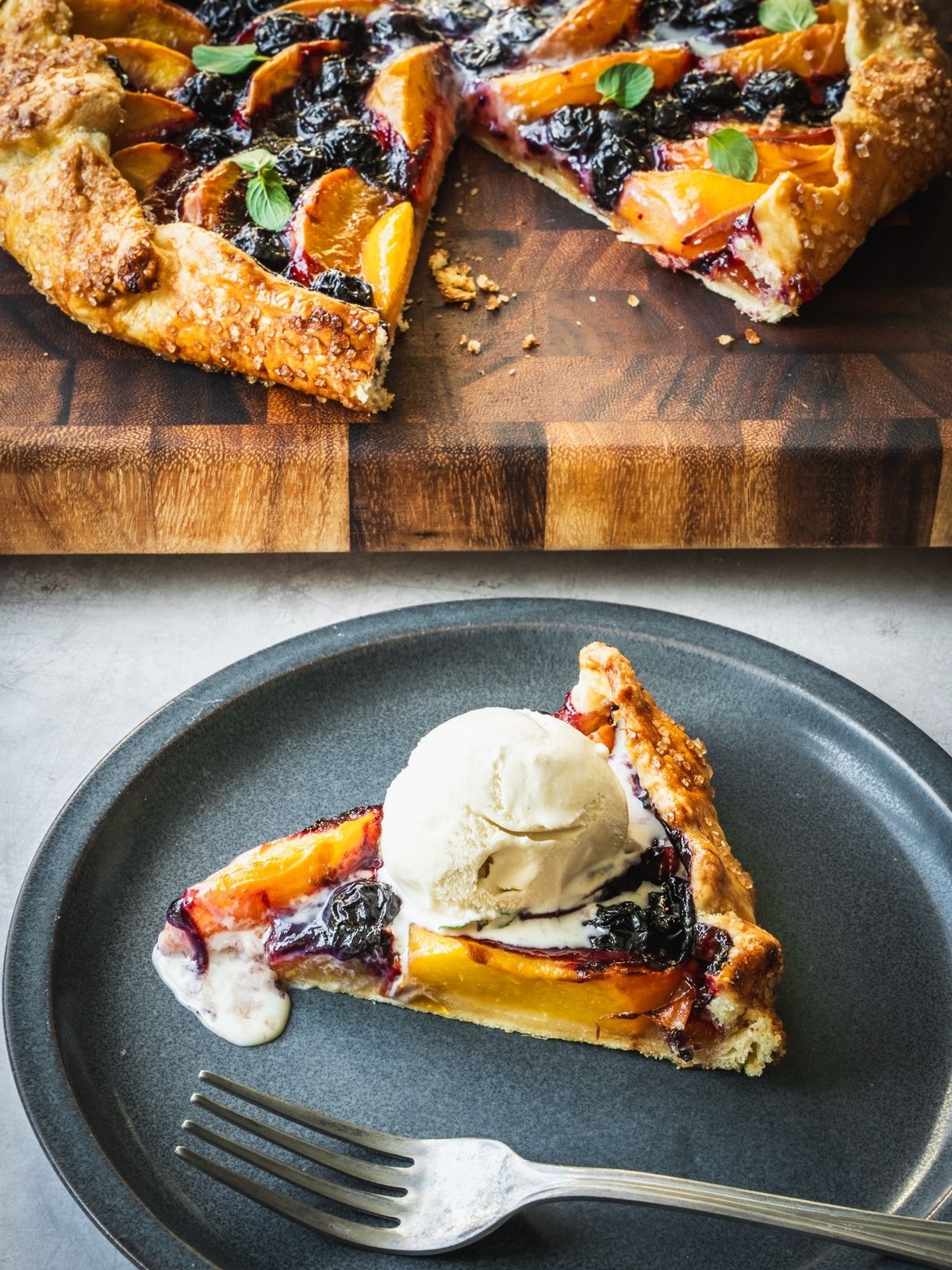 Slice of blueberry peach galette on a plate with a scoop of ice cream. 