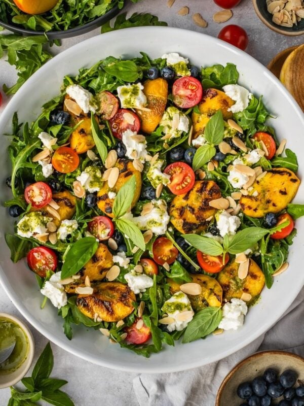 Grilled peach salad with basil, arugula, blueberries and goat cheese in a large serving tray.